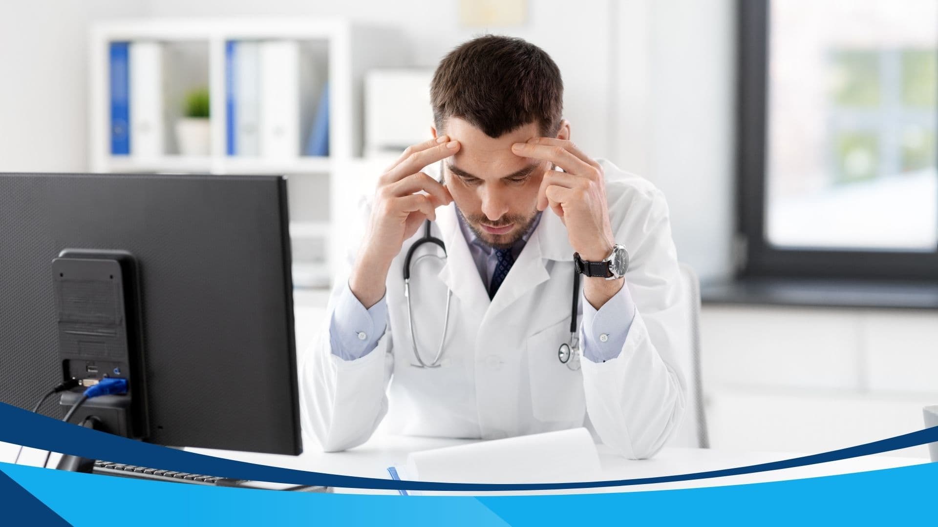 A stressed doctor in a white lab coat sits at a desk with a computer monitor, resting his head in his hands. A stethoscope hangs around his neck, and a modern office with shelves and a window is in the background.
